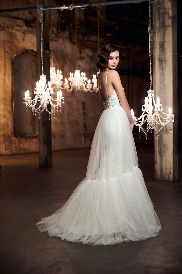 Bride in room with chandeliers, ornate looking, two-tiered dress displayed on model