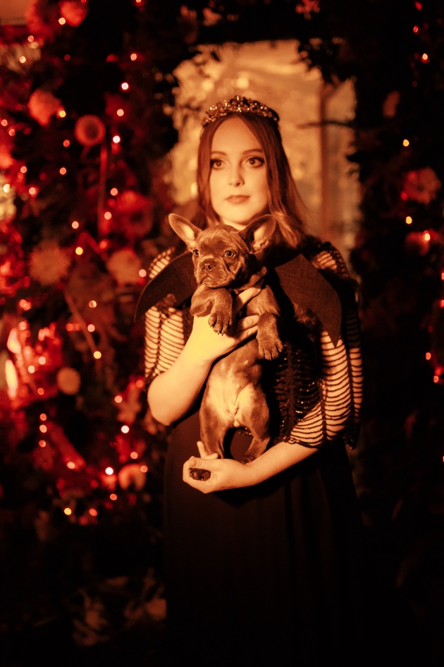 Woman wearing black dress and tiara holding a French Bulldog puppy