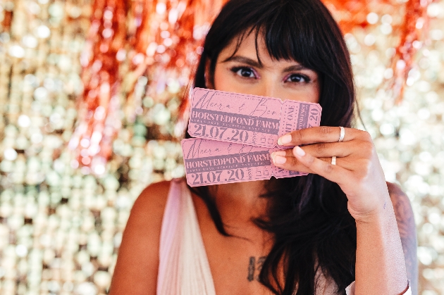 bride holiding festival ticket-style wedding invitations in front of her face