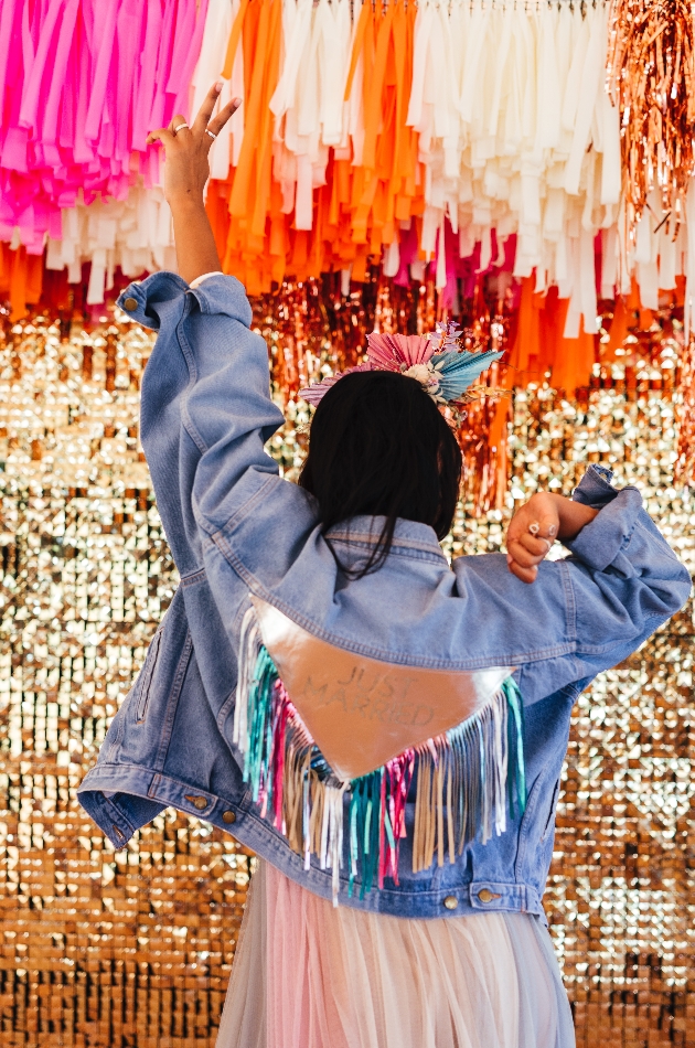 Bag of bride wearing a customised denim tassel jacket which reads 'just married'