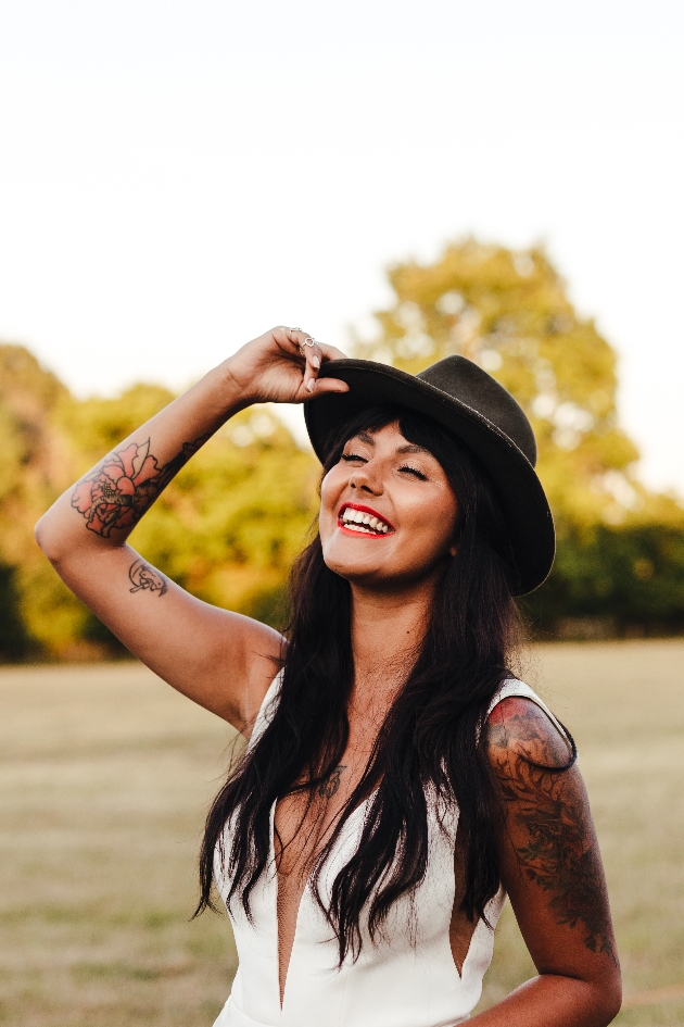 Bride in a field laughing and touching the brim of her hat