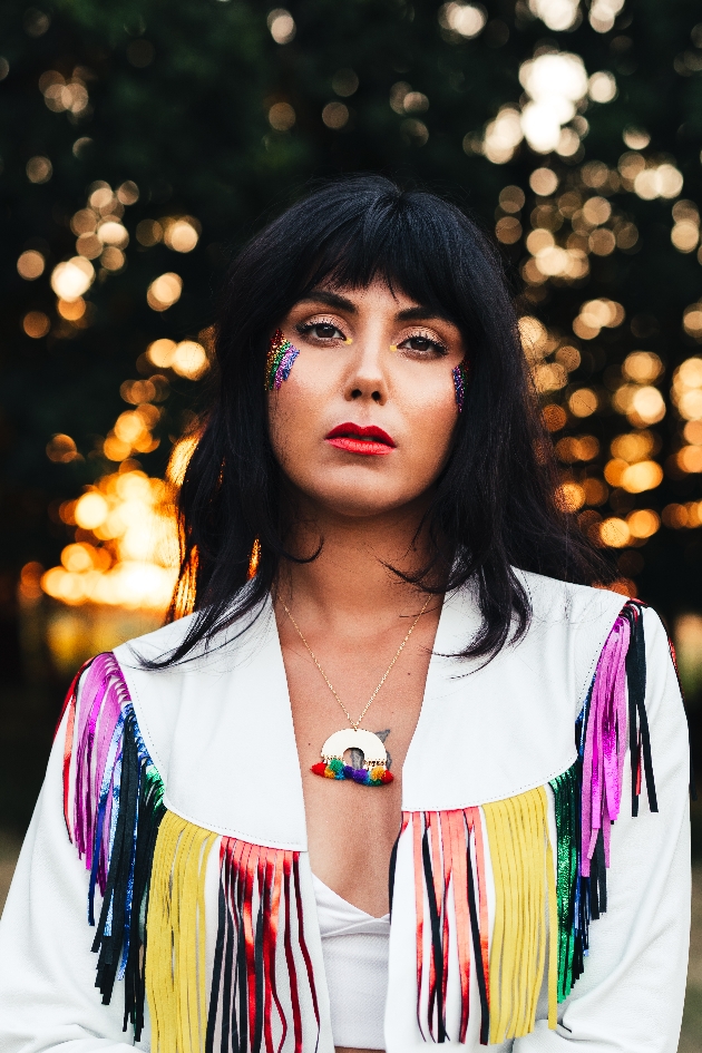 Festival bride with rainbow glitter on her cheeks wearing a rainbox tassel white jacket