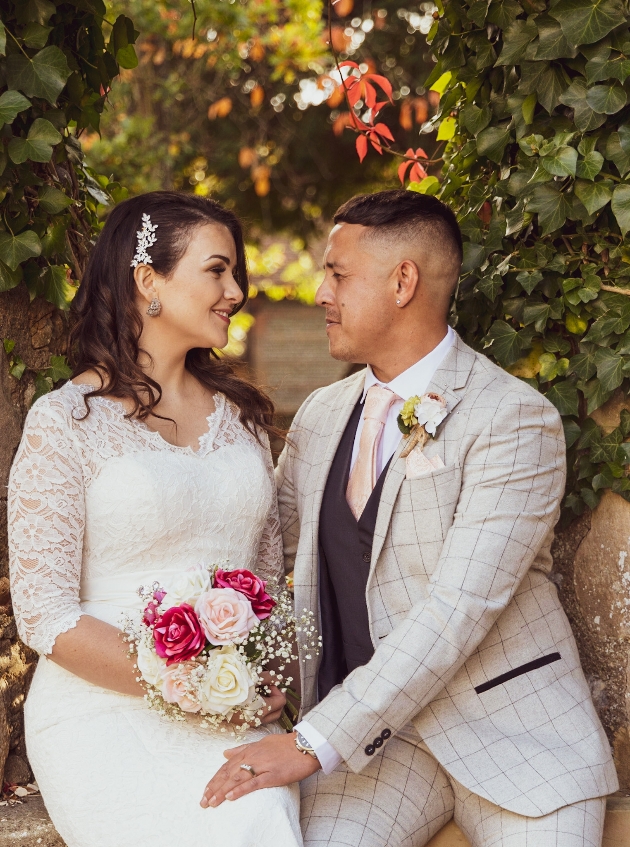 Bride and groom sitting on a wall and gazing into each others eyes