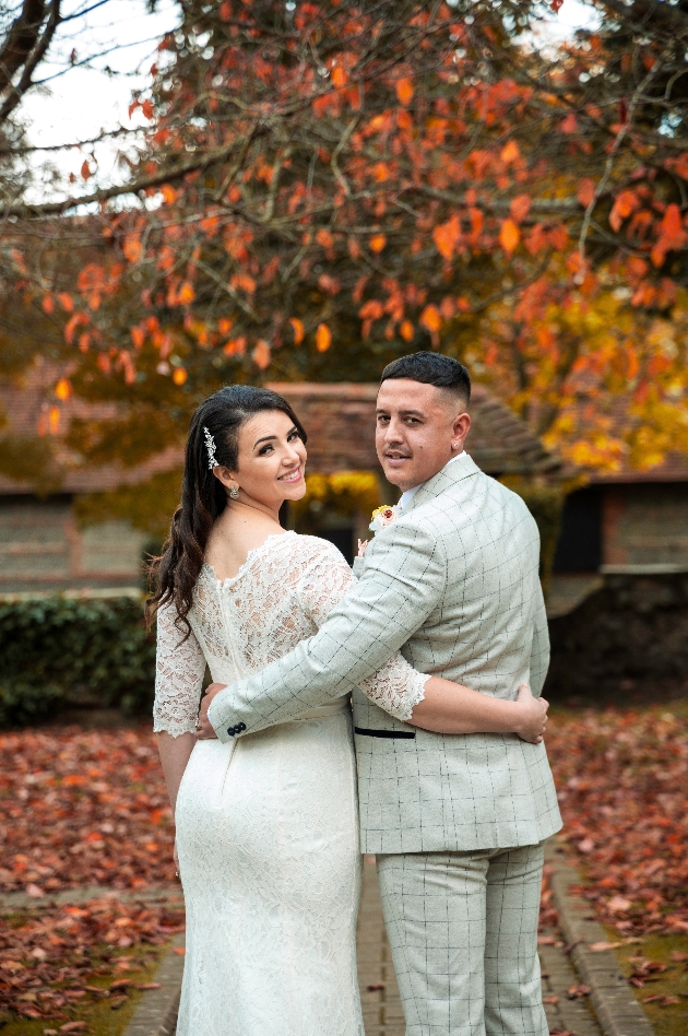 Bride and groom with their backs to the camera and arms around each other look back over their shoulders