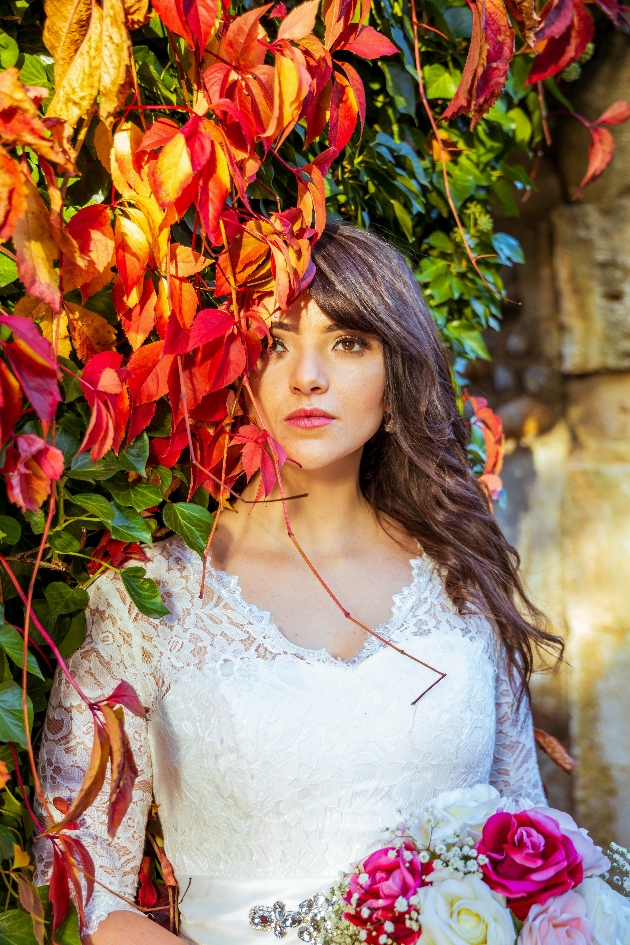 beautiful bride partly obscured by autumn leaves