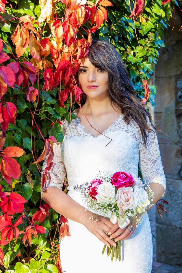 longer shot of bride obscured by autumn leaves holding pink and white bouquet