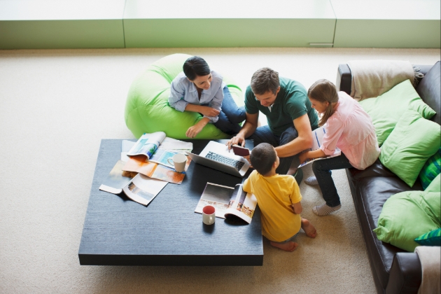 Two adults and two children on floor in lounge area looking at a laptop