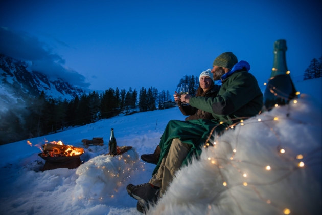 couple in ski gear at night snuggled round a camp fire