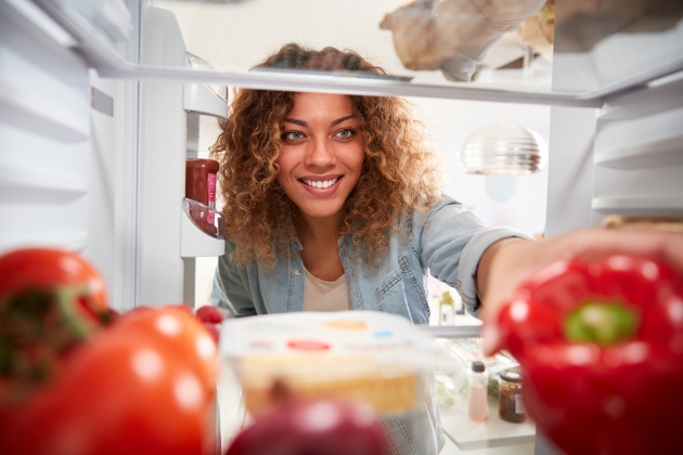 Woman reaching into the fridge for a red pepper