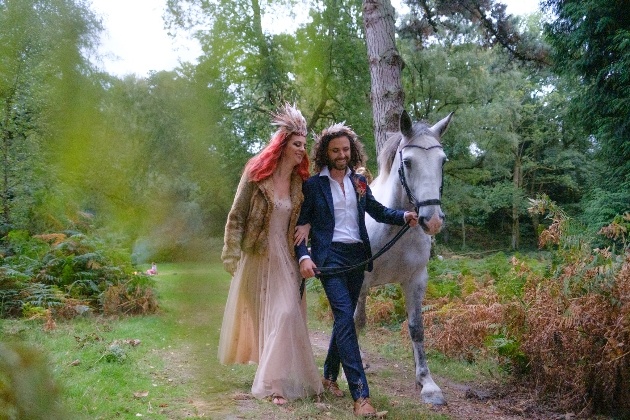 Couple walking through the woods with a white horse. 