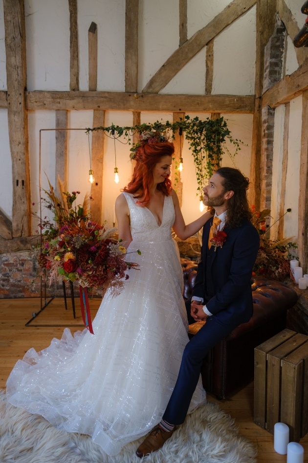 Bride and groom in wedding barn looking at each other bride holds autumnal bouquet