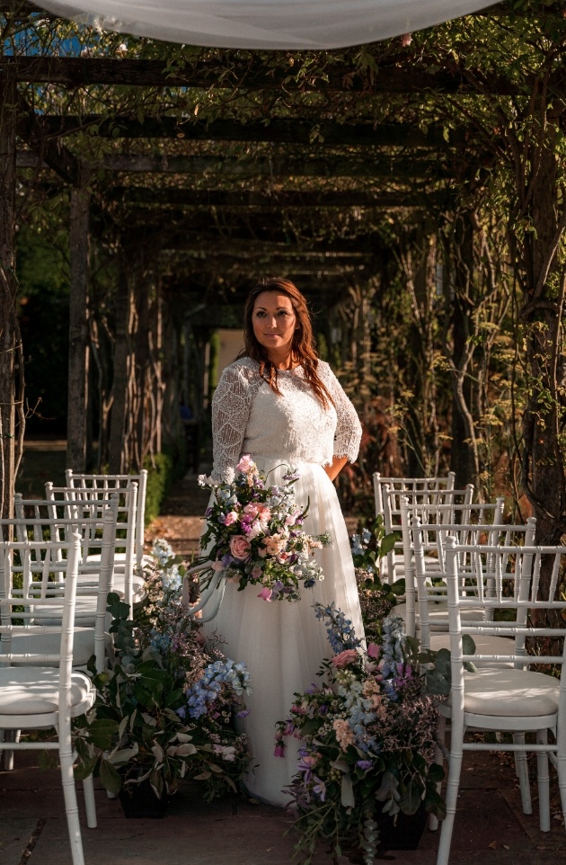bride standing underneath wedding ceremony covered area dressed in english wildflowers