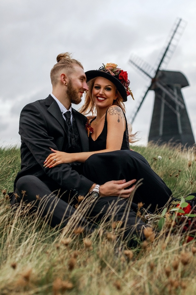 bride and groom sat on the grass in front of windmill