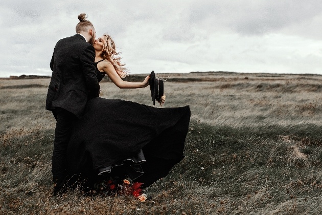 bride and groom dresse in black kissing. Bride's skirt is caught by the wind