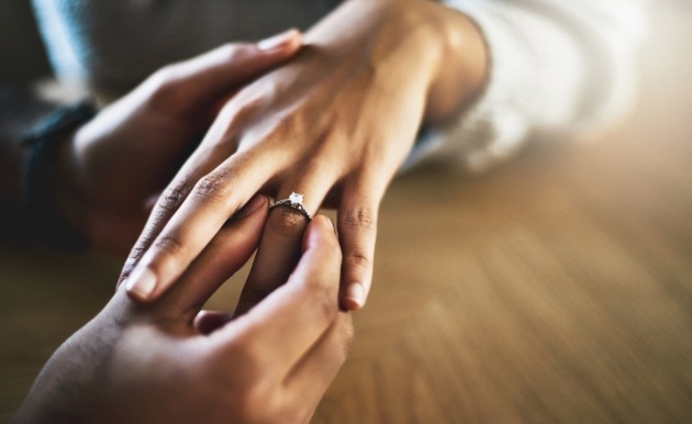 two hands one putting an engagement diamond ring on the other 