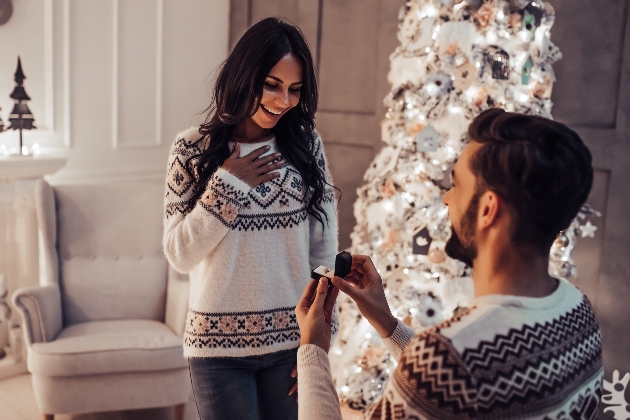 couple getting engaged in front of christmas tress
