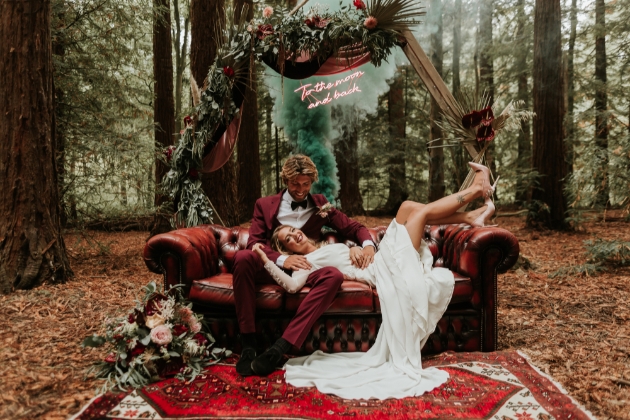 bride and groom chilling on sofa with moongate and neon sign in the background woodland wedding setting