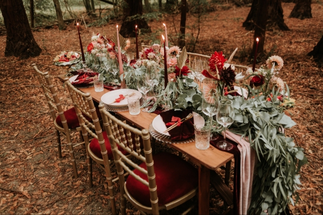 wedding breakfast table set up in woodland setting with lit candles and floral runner