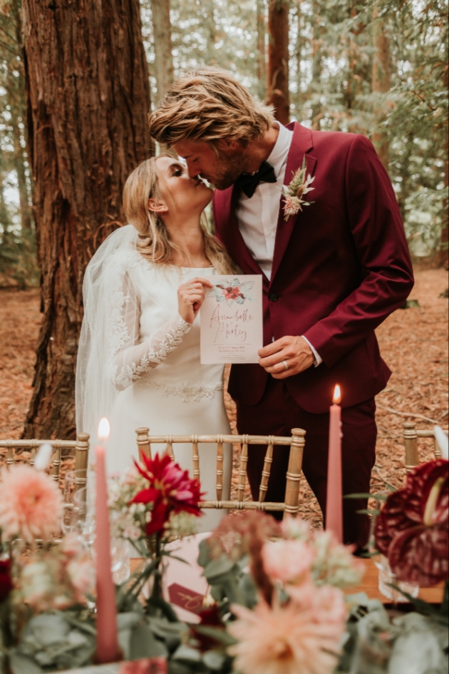 bride and groom kissing and holding up their wedding stationery