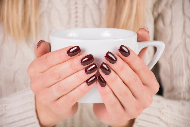 woman wearing dark nail polish for the winter cupping her hands around a mug of hot drink