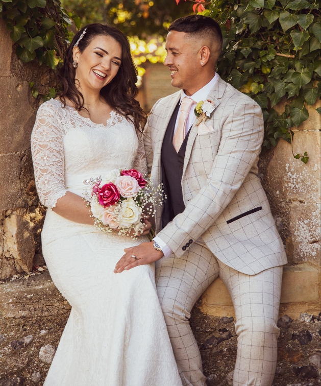 Bride and groom sitting on a wall laughing