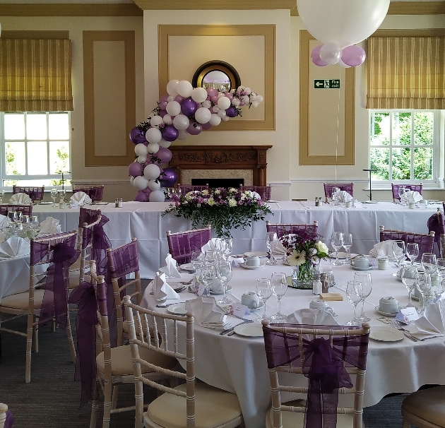 Wedding reception with plum palette, balloons, chair sashes and balloon crescent arch