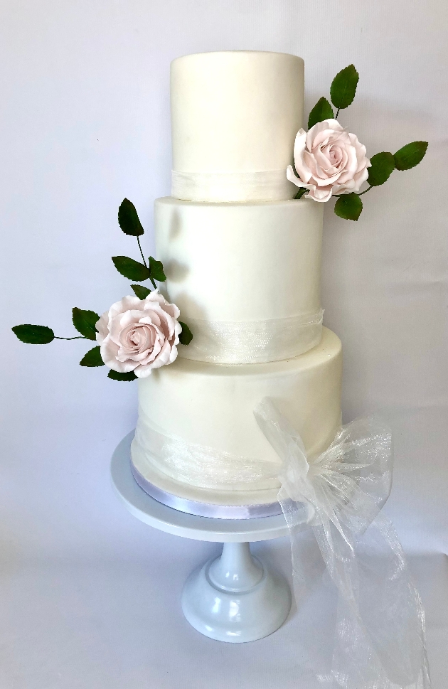 Three tier white wedding cake with pink sugar flowers