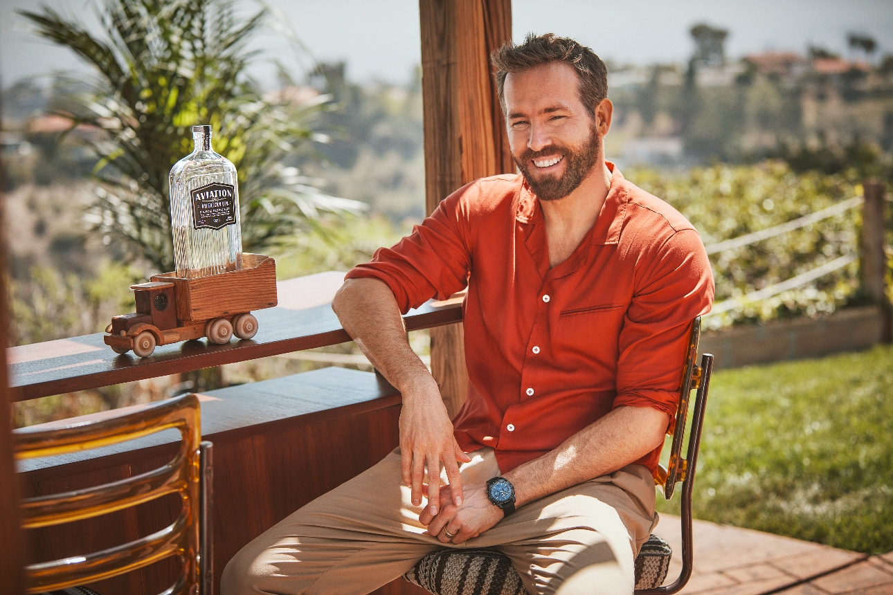 Ryan Reynolds sat by a pool bar with a bottle of gin on the counter