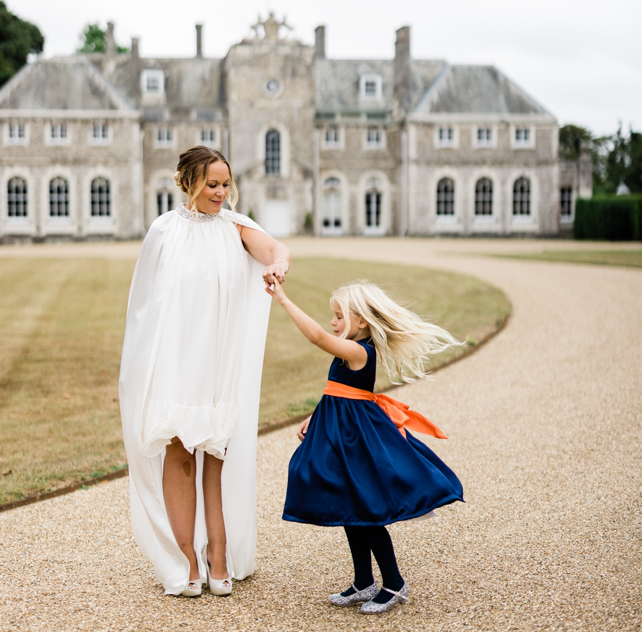 bride outside manor house twirling bridesmaid in dress