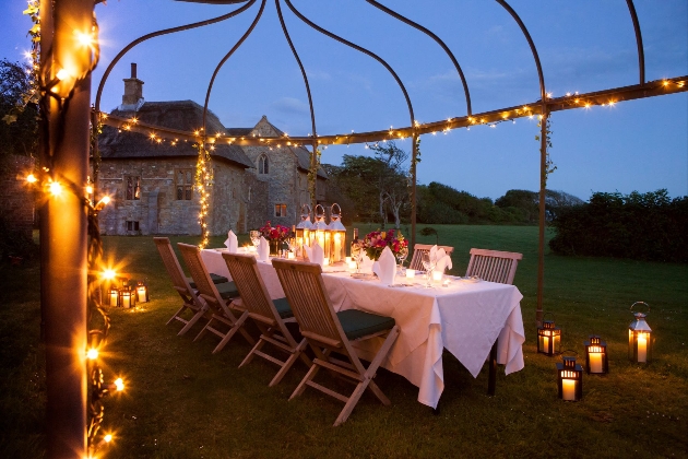 A dinner table set up outside underneath fairylights