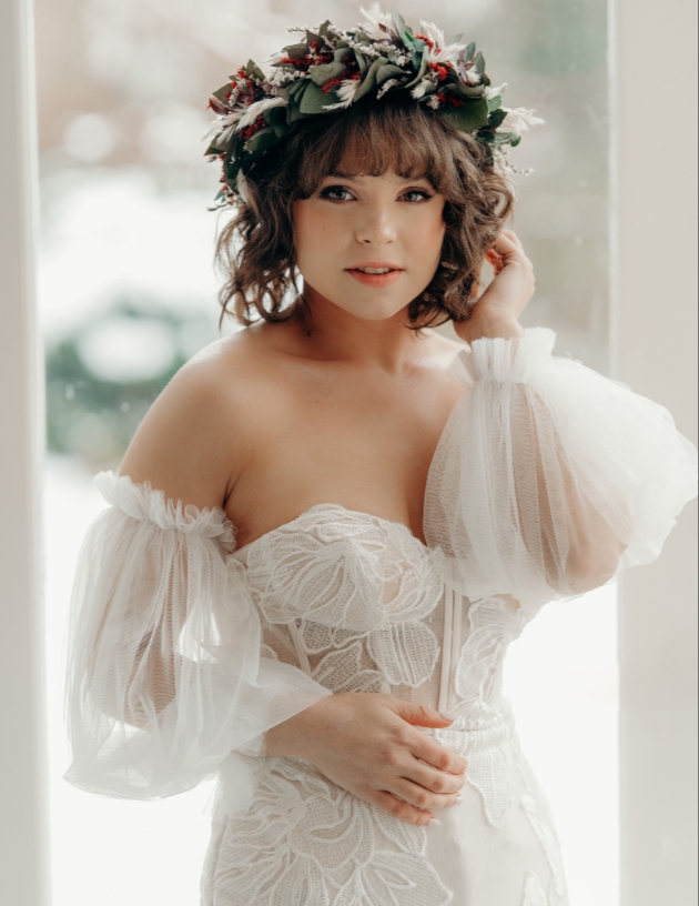 Boho bride standing in front of window wearing flower crown and puff sleeve dress