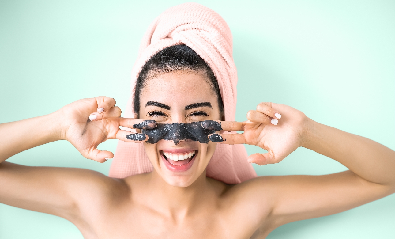 model with hair towel on, with moisturiser on her hands wiping it on her face 