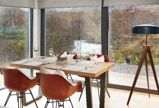 Four orange chairs placed around a dining table that looks out over Scottish countryside