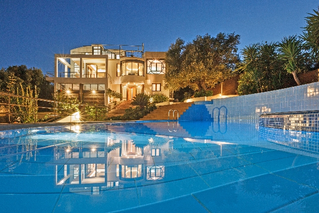 A swimming pool with a well lit villa in the background