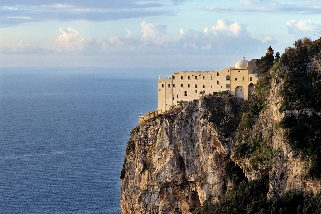 The exterior of a monastery close to the edge of a cliff overlooking the sea