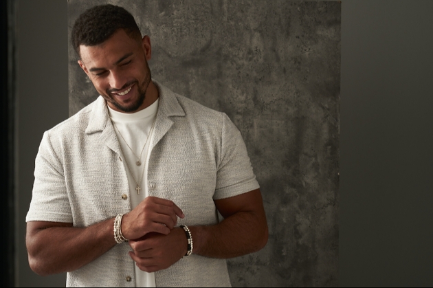 A man smiling while wearing a cream shirt and several bracelets