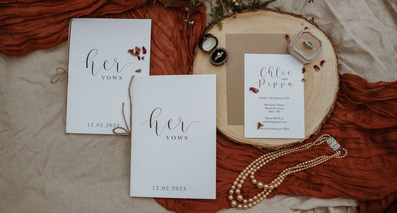 vow booklet on material displayed on log with necklace and ring near
