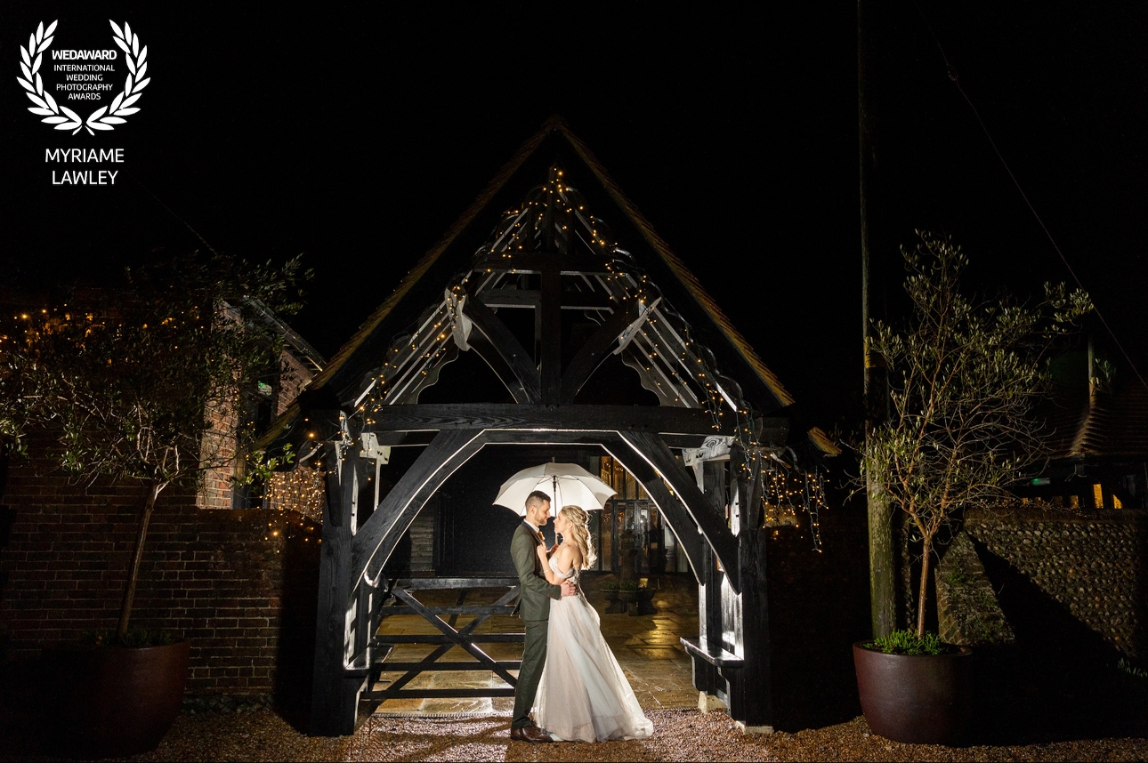 bride and groom at night in the rain under an arch