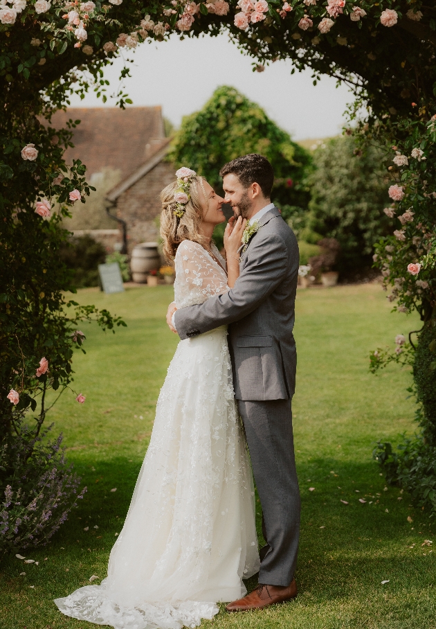 Bride and groom beneath floral archway at Pangdean Old Barn