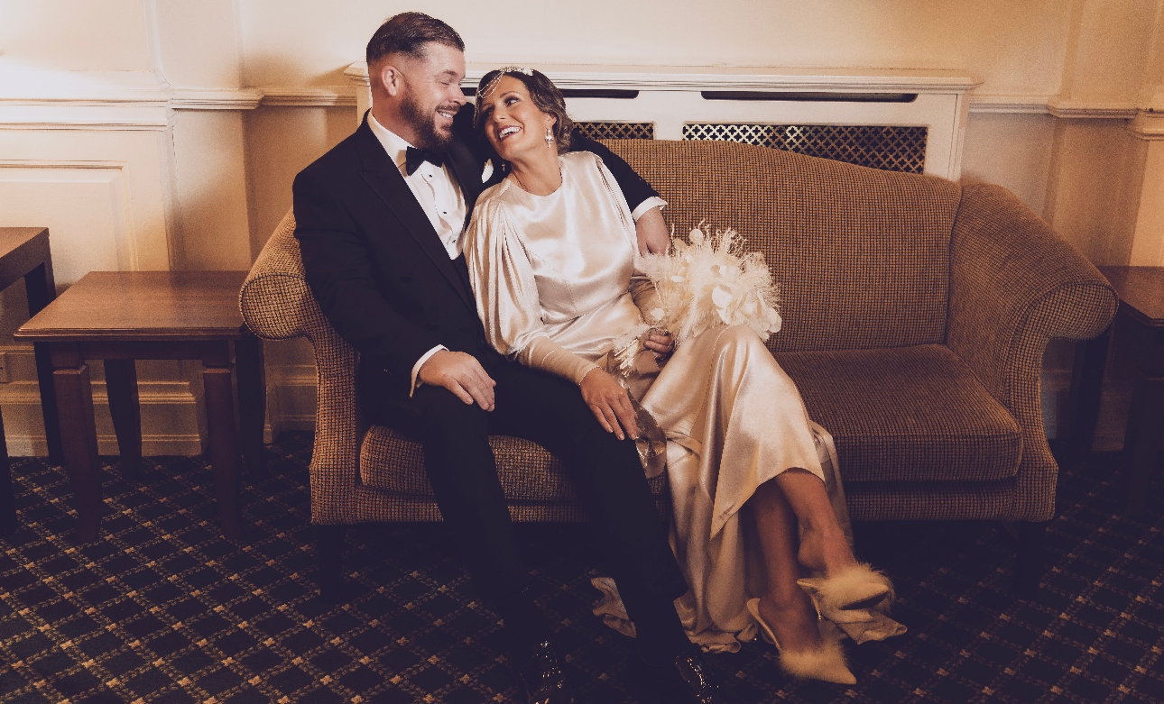 bride and groom dressed in 1920s vintage attire laughing on sofa