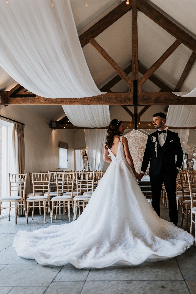 ceremony space with white draping and fairylights. Bride and groom holding hands