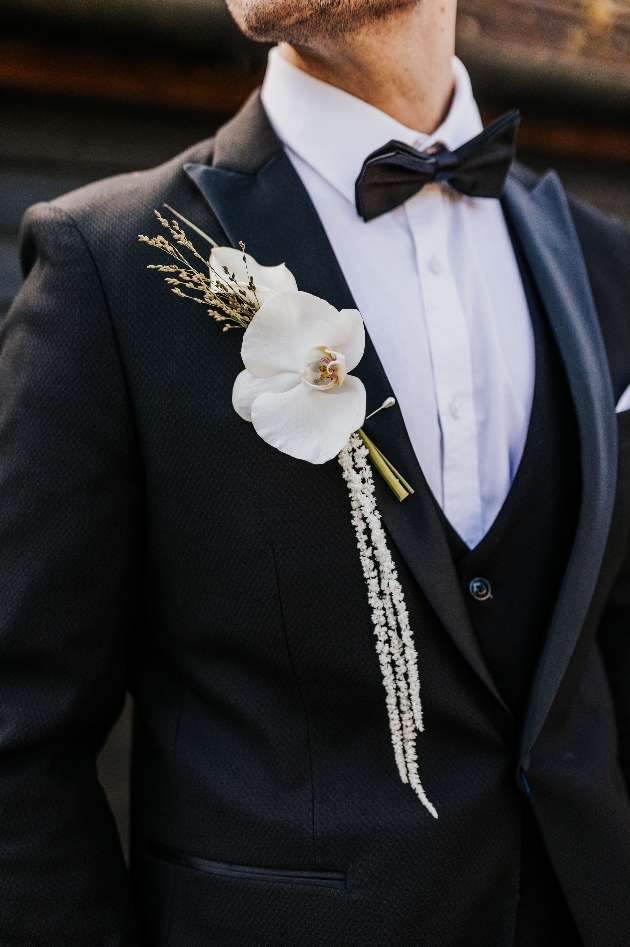 groom wearing black tux with bowtie and orchid buttonhole