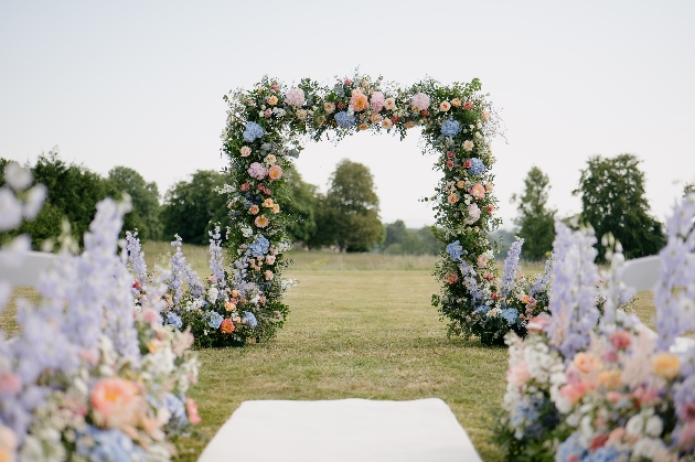 outdoor wedding ceremony setup, square floral arch in palette of pastels, meadow aisle flowers